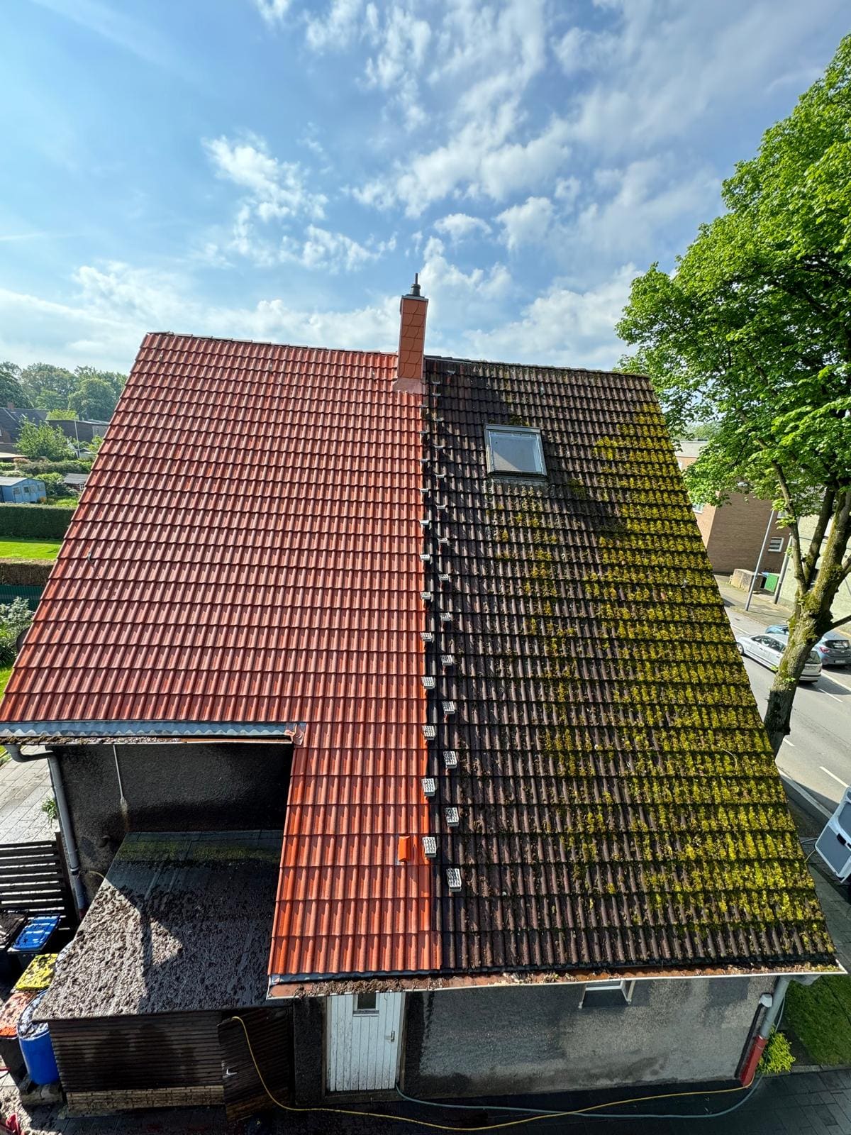 Dachreinigung in vollem Gange: eine Dachhälfte bereits leuchtend rot, die andere noch moosbewachsen